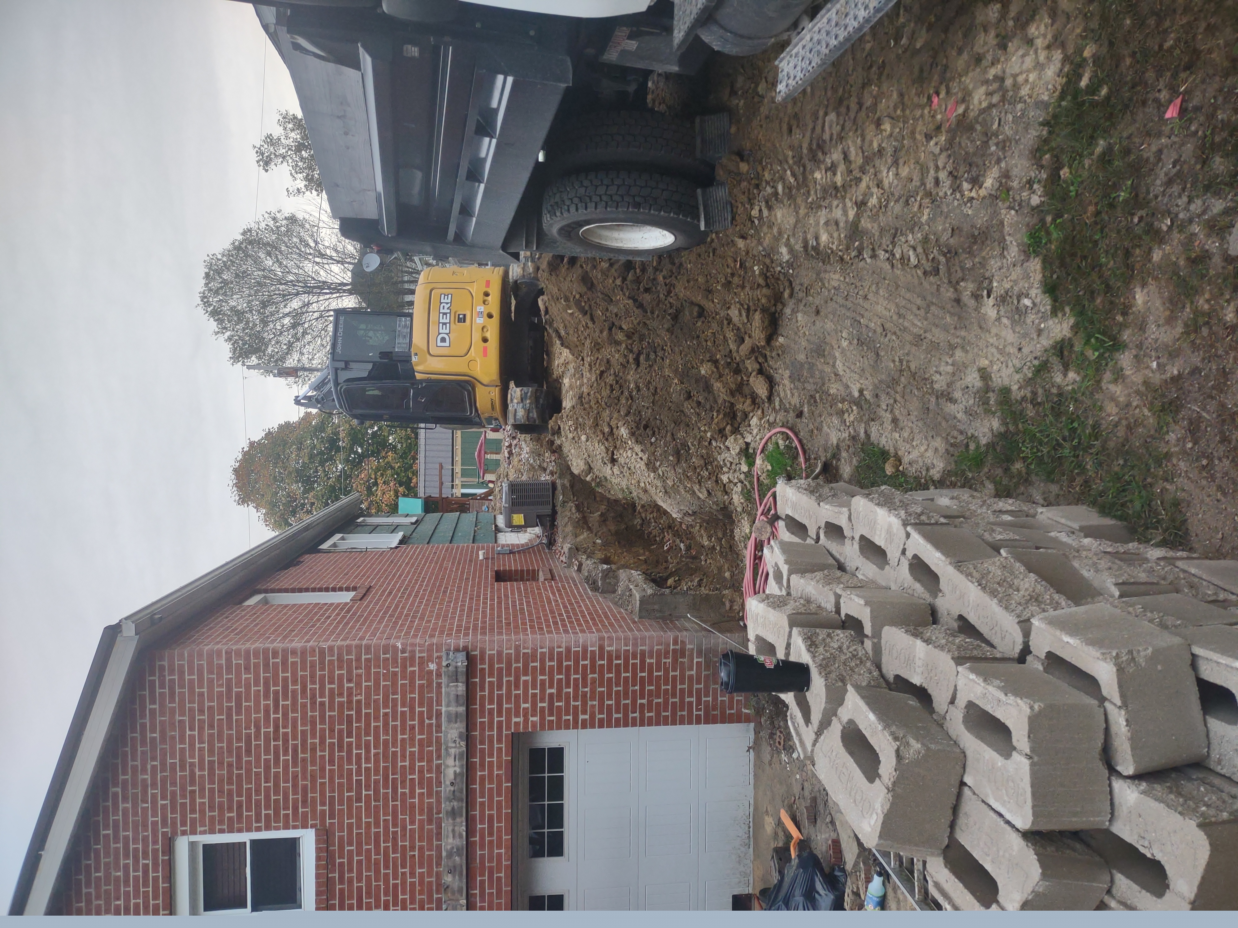 Excavation alongside brick home with John Deere mini ex and dump truck