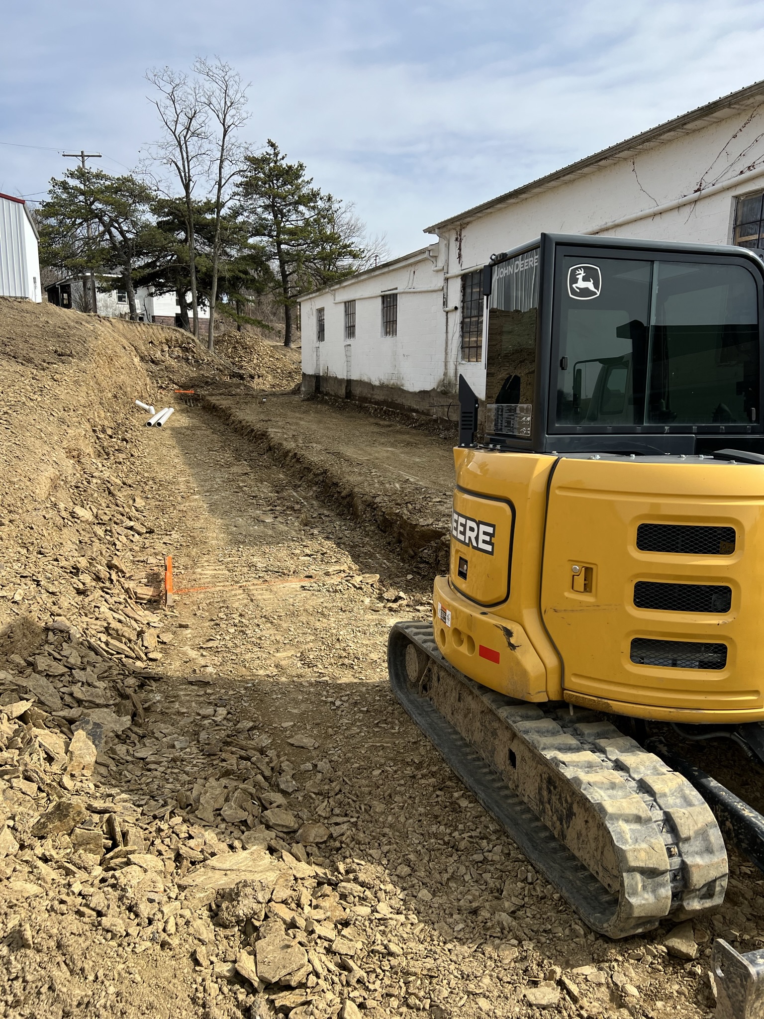 John Deere mini ex working trench alongside white block building