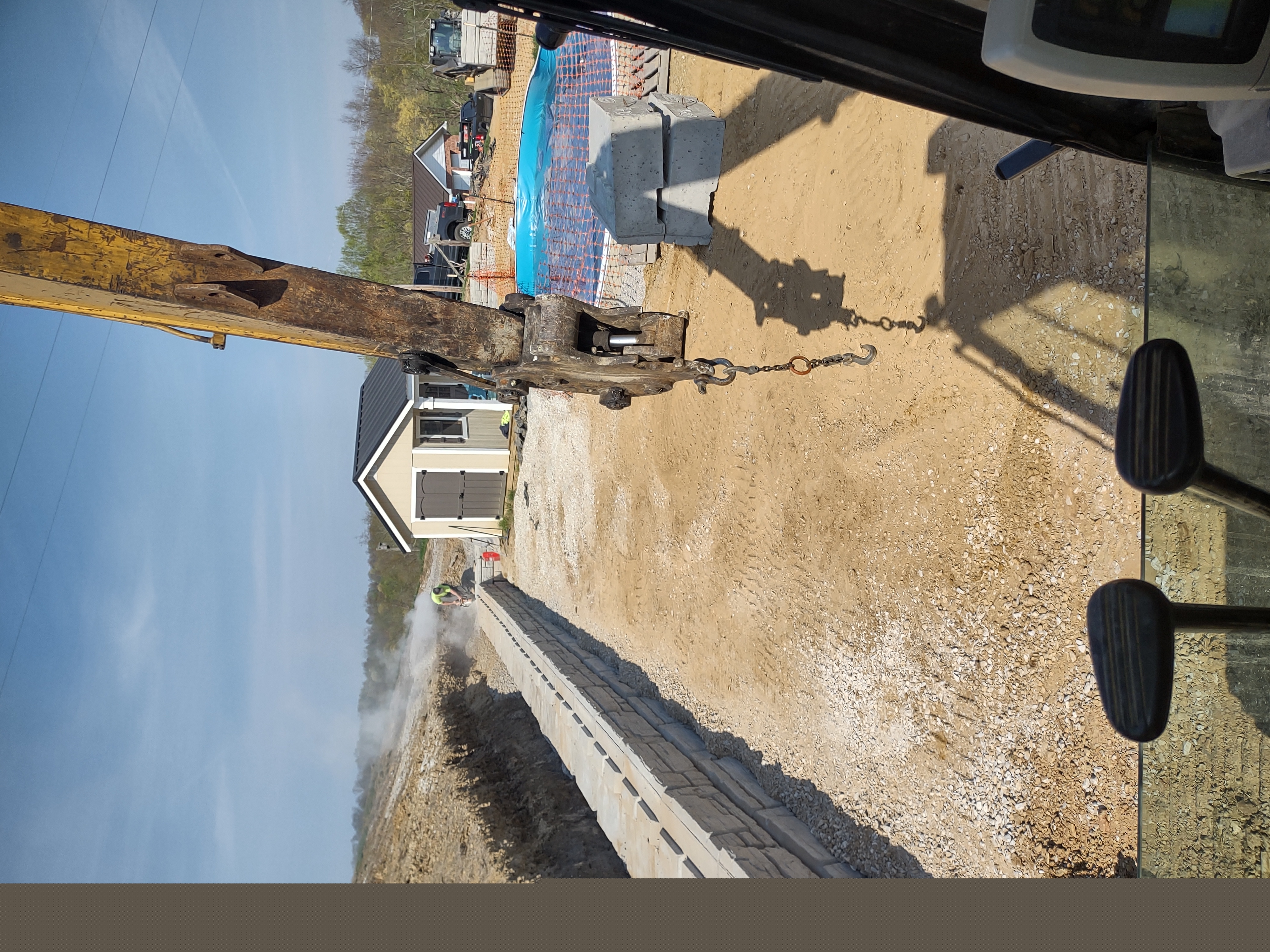 CAT excavator working retaining wall area with pool covered in background