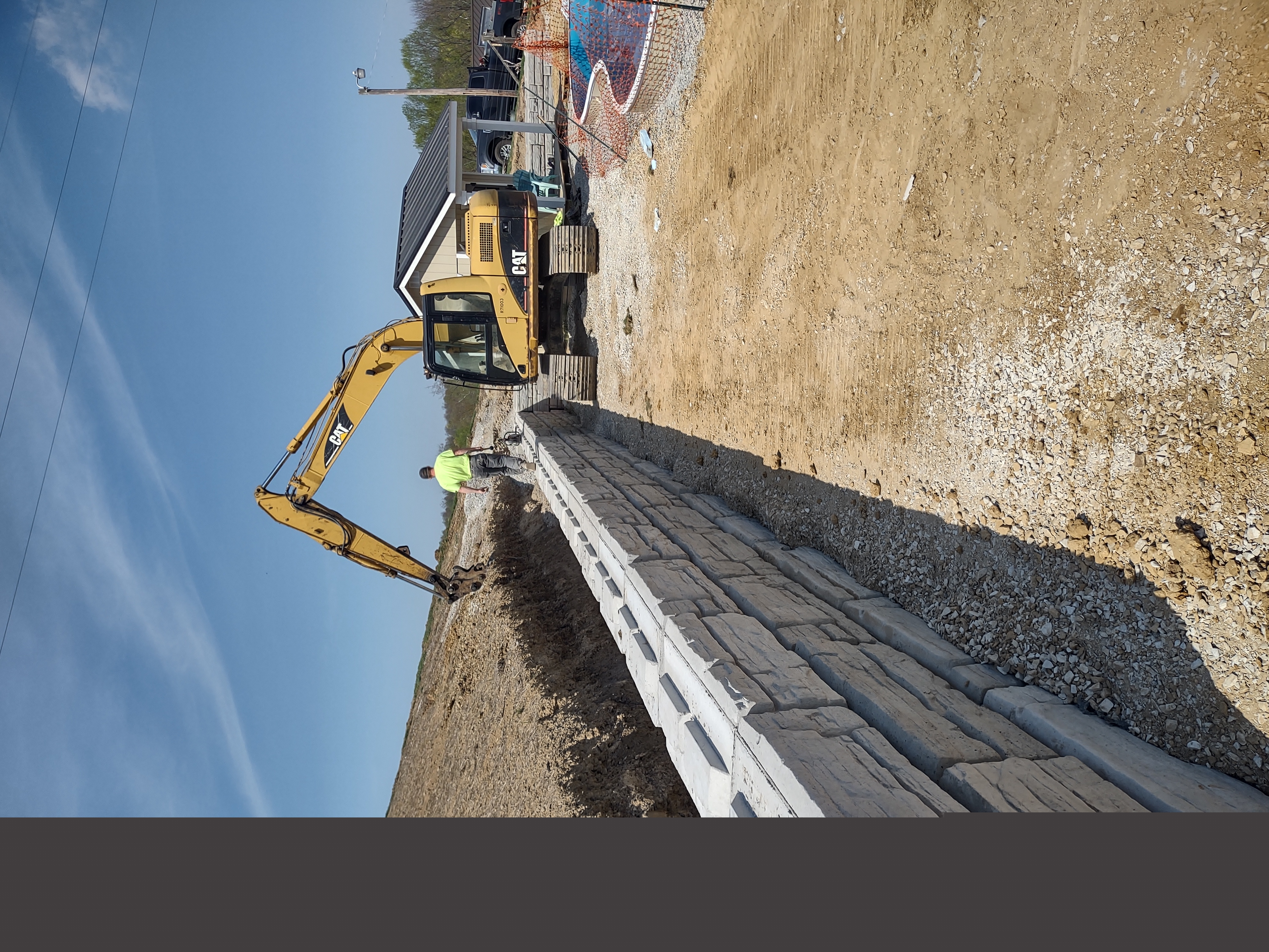 Long stone retaining wall with CAT excavator and crew backfilling