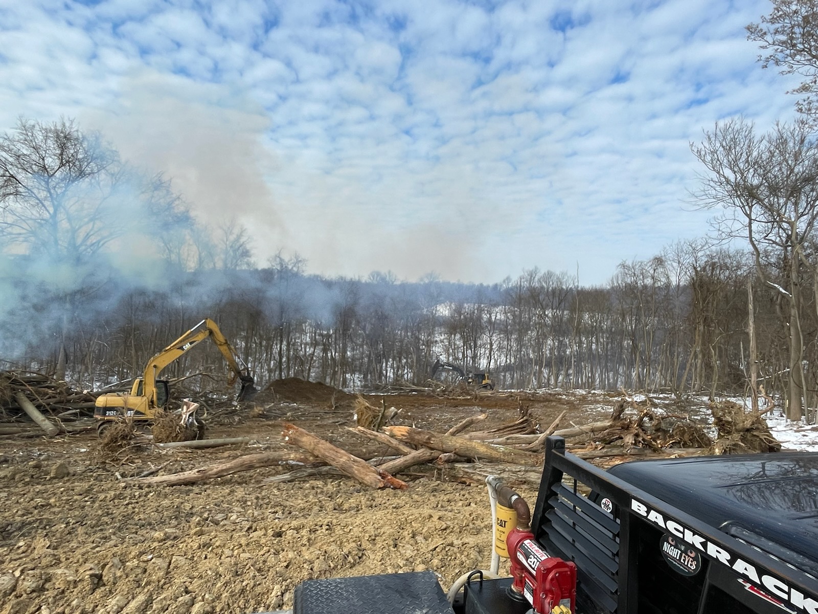 CAT 312 and second machine clearing trees with burn pit smoke
