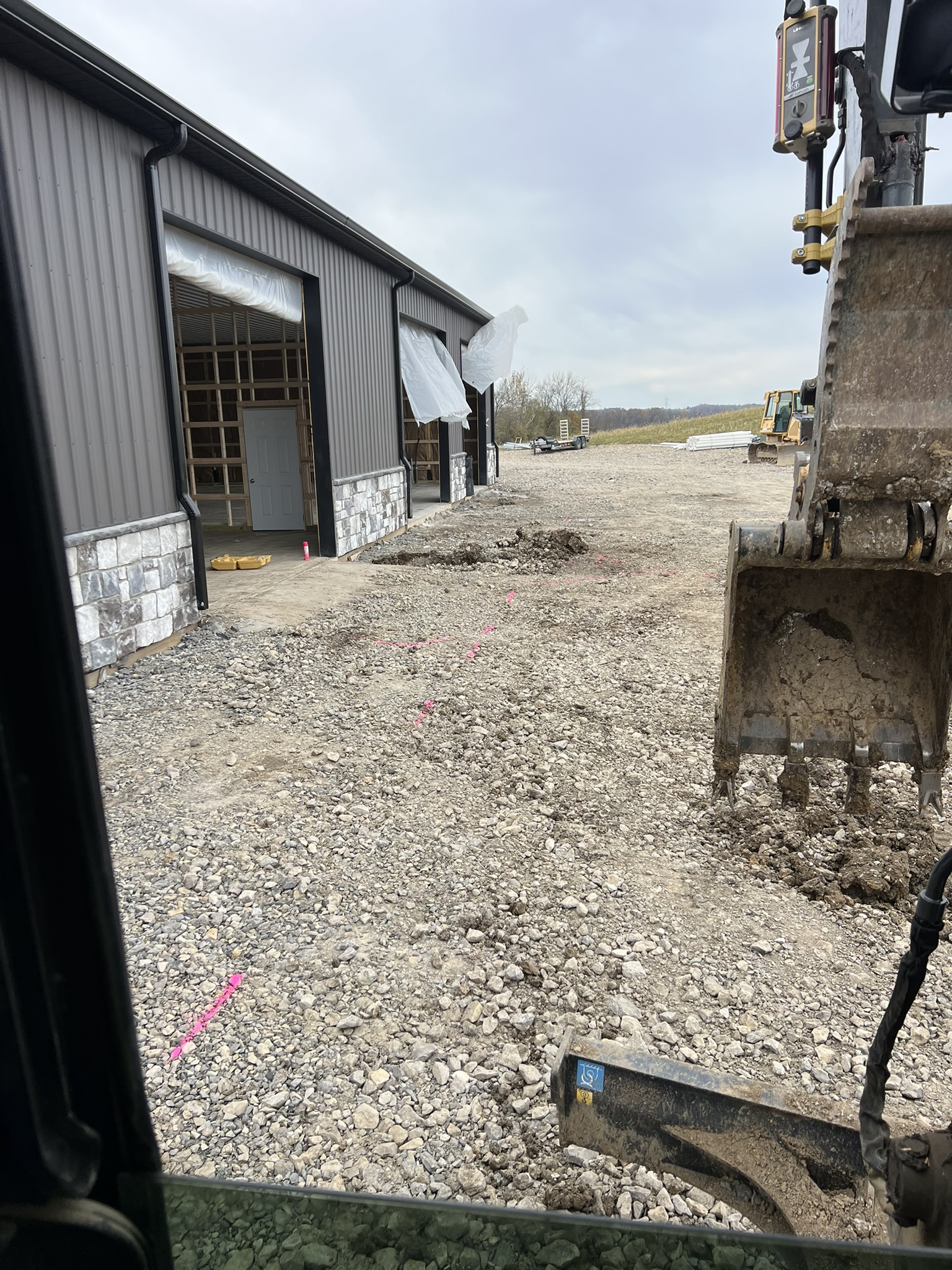 Excavator working utility trench alongside barn