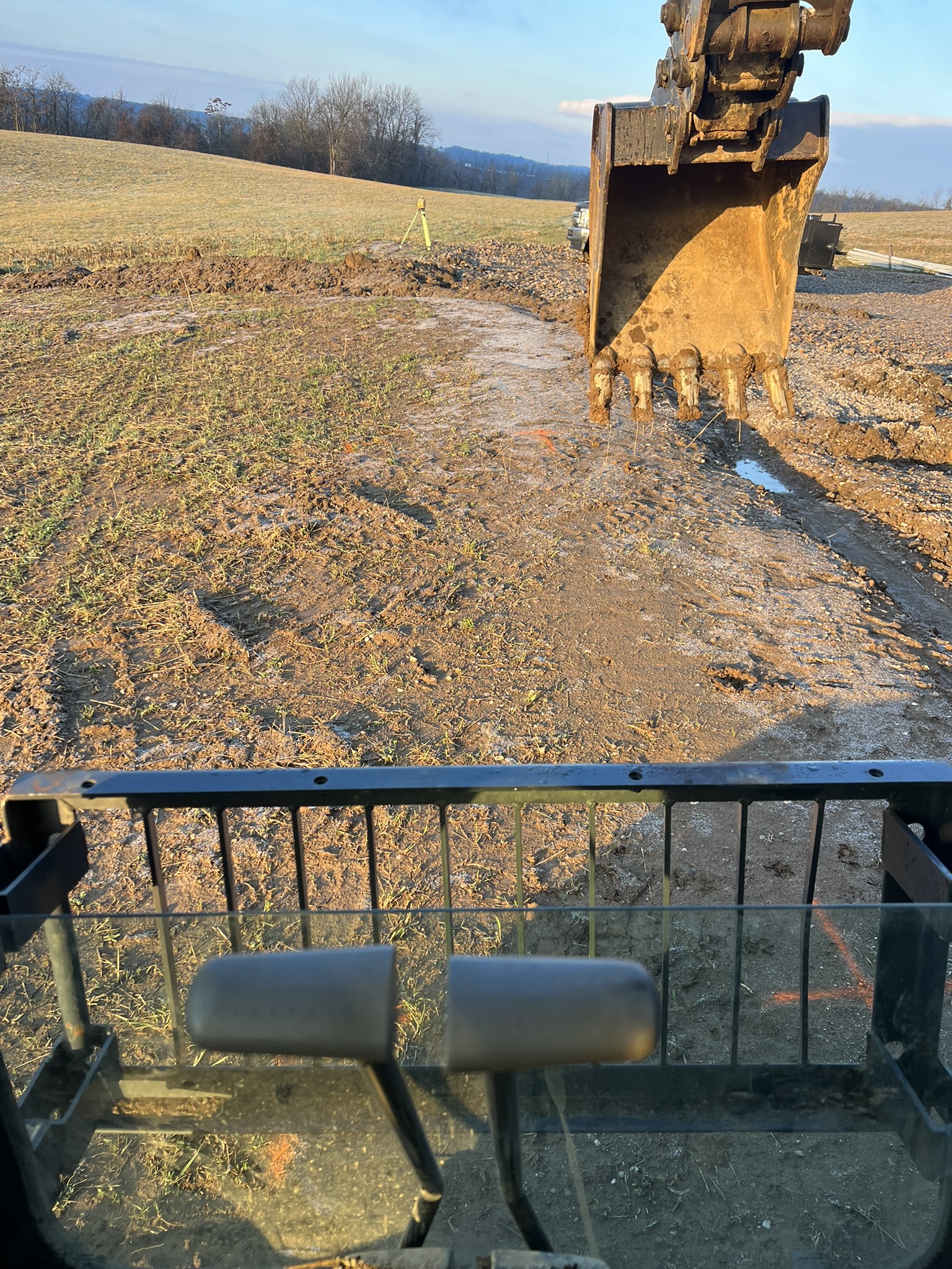 Excavator trenching in farm field with laser level