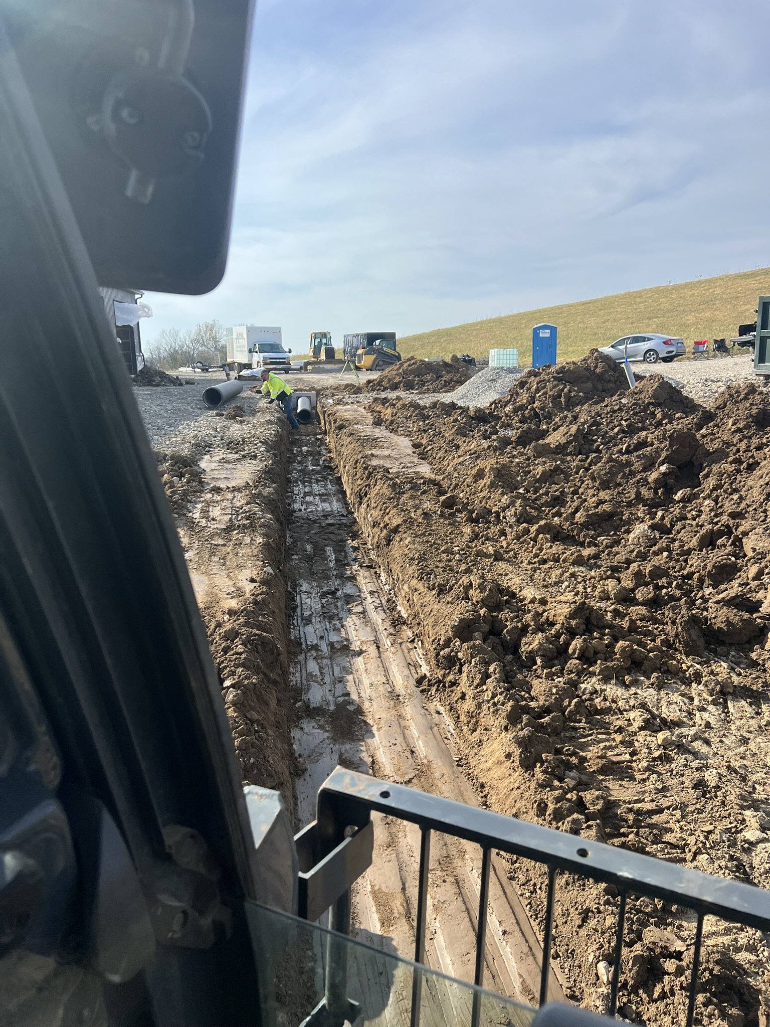 Long utility trench cab view with crew installing pipe