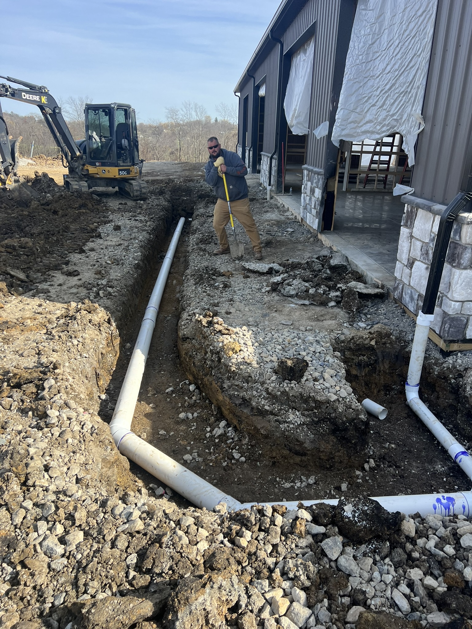 Crew hand-grading trench alongside barn