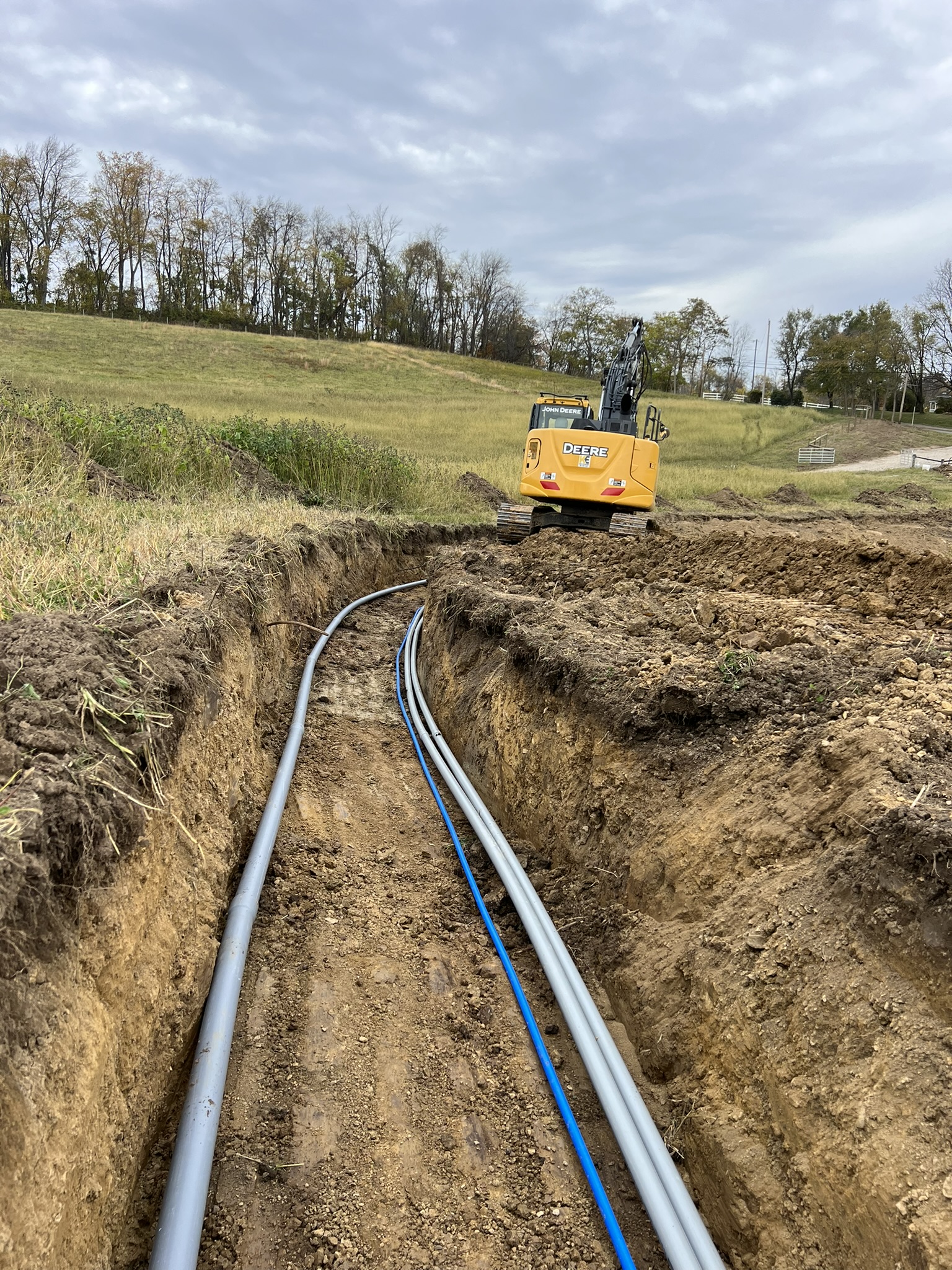 John Deere excavator continuing conduit trench up hill