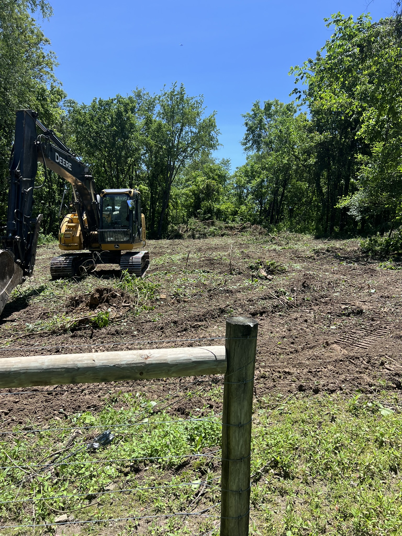 John Deere excavator working cleared area along fence line